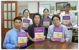 チェンマイ市にあるLink事務所にて「村の百科事典」を手に取るLinkのスタッフと水野代表